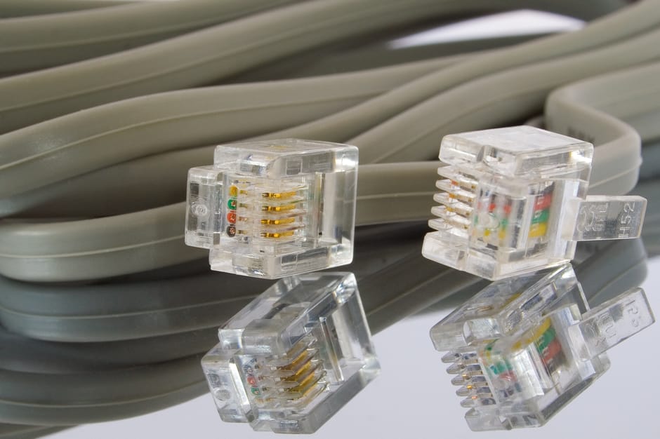 A close-up view of several transparent Ethernet cables with gold-plated connectors resting on top of a coiled grey cable, positioned on a reflective surface. The cables are inside a property, near an